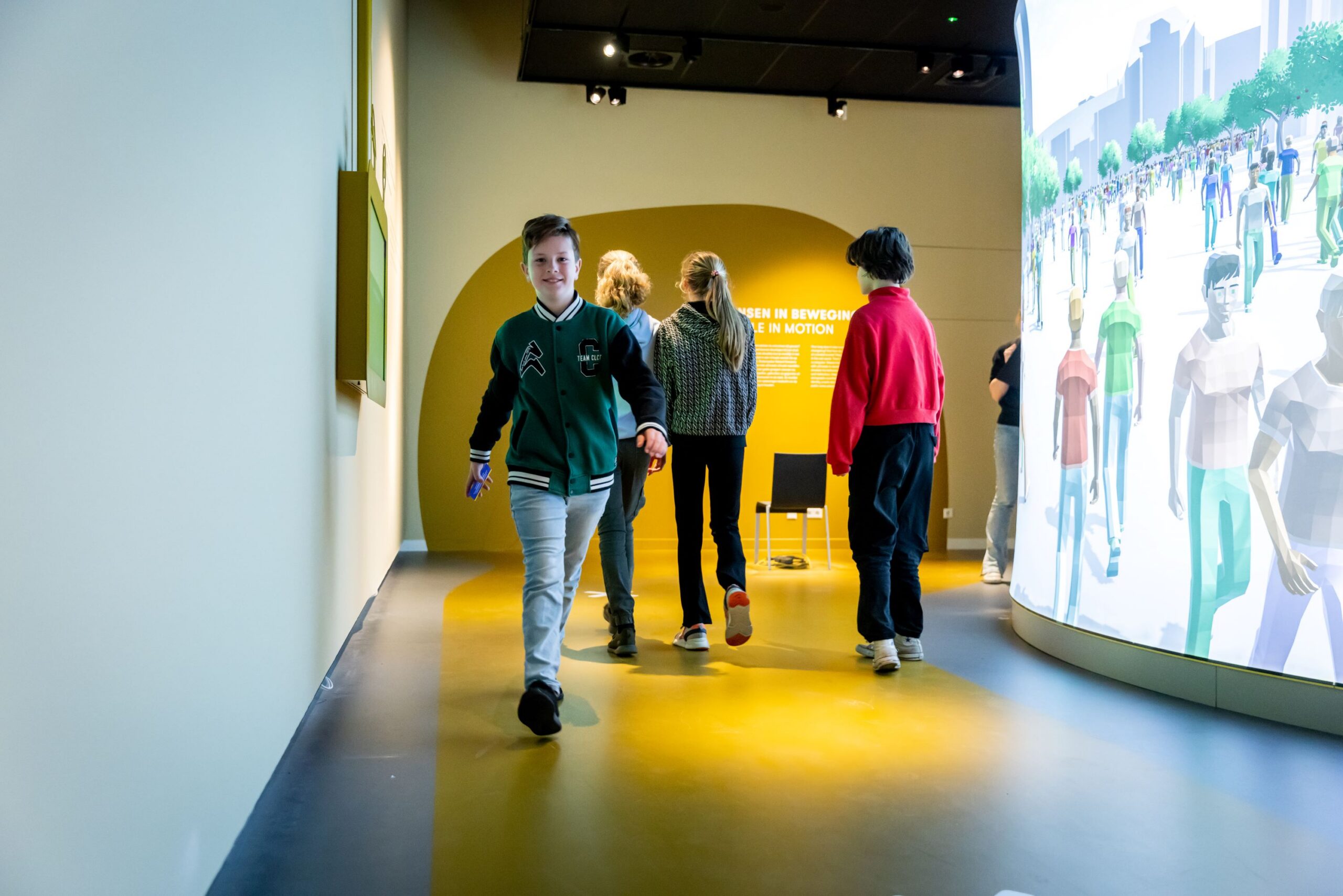 Een leerling loopt door de zaal van 'Alle mensen verzamelen'. Achter hem staan twee andere leerlingen.